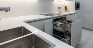 A close-up of a 'magic corner' pull-out unit in a sleek, grey Bangladeshi kitchen, maximizing storage for spices and pots.
