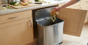 Exposed free-standing plastic trash bin in a kitchen prep area causing clutter.